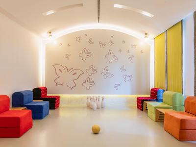 Moderner, heller Raum mit farbigen Sitzwürfeln, Schmetterlingsbildern an der Wand und großen Fenstern.