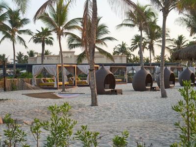 Strandbereich mit Hängematten und Sitzgelegenheiten zwischen Palmen an einem Resort.