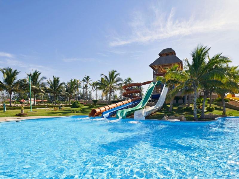 Wasserpark mit großen Rutschen, klarem blauen Pool und Palmen bei sonnigem Himmel.