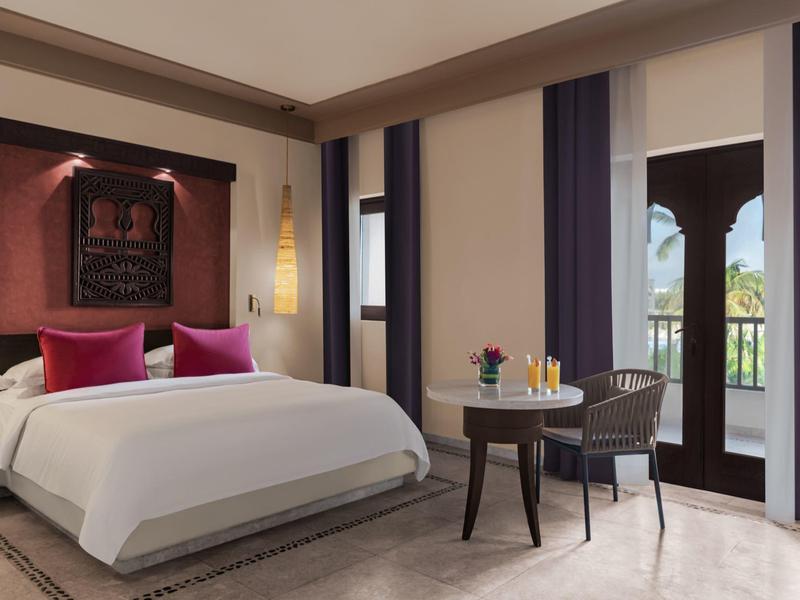 Elegantes Schlafzimmer mit großem Bett, lila Kissen, dunklen Vorhängen und Balkonzugang.