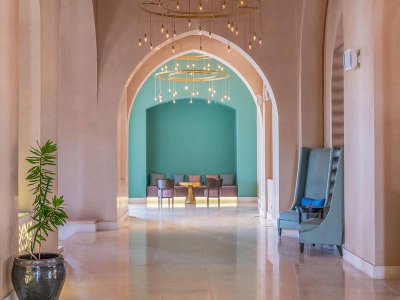 Ein heller Gang mit hohen Bögen, Pflanzen und einem Sitzbereich in der Ferne mit blauer Wand.