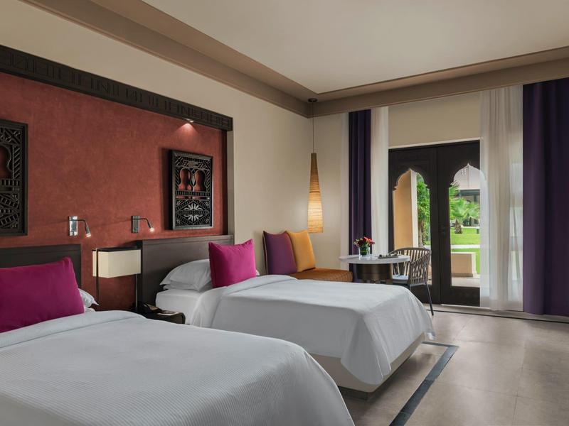 Modernes Hotelzimmer mit zwei Einzelbetten, farbigen Kissen und Blick auf die Terrasse.