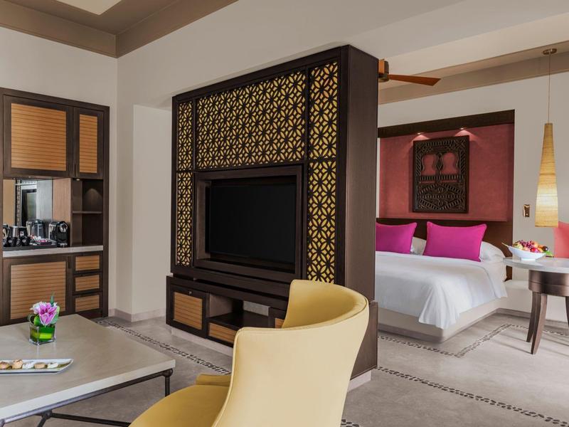 Moderner Wohnbereich mit gelbem Stuhl, Fernseher, Blumen auf Tisch und angrenzendem Schlafzimmer.