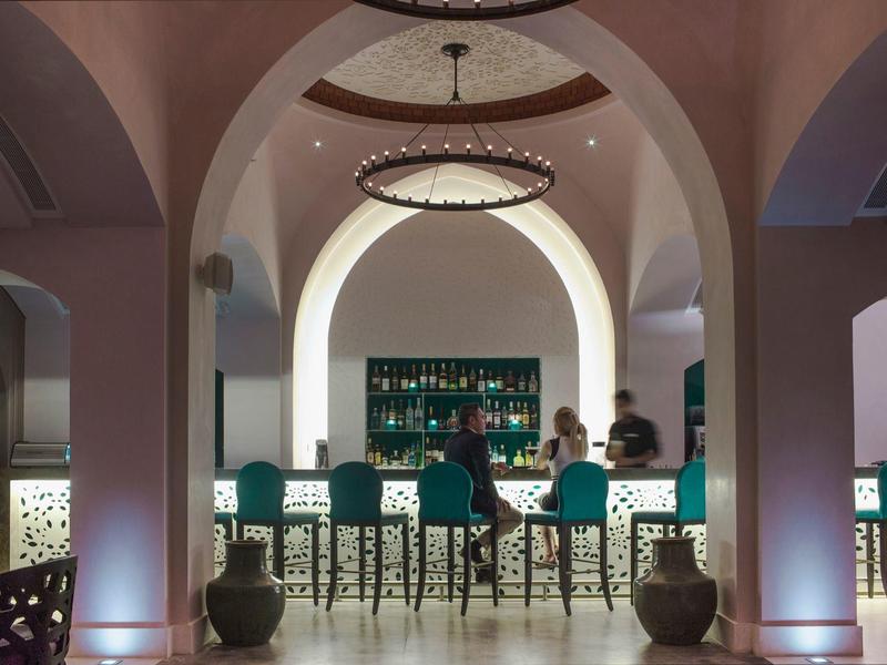 Elegante Bar mit Rundbögen, blau beleuchteten Stühlen und zwei Personen am Tresen.