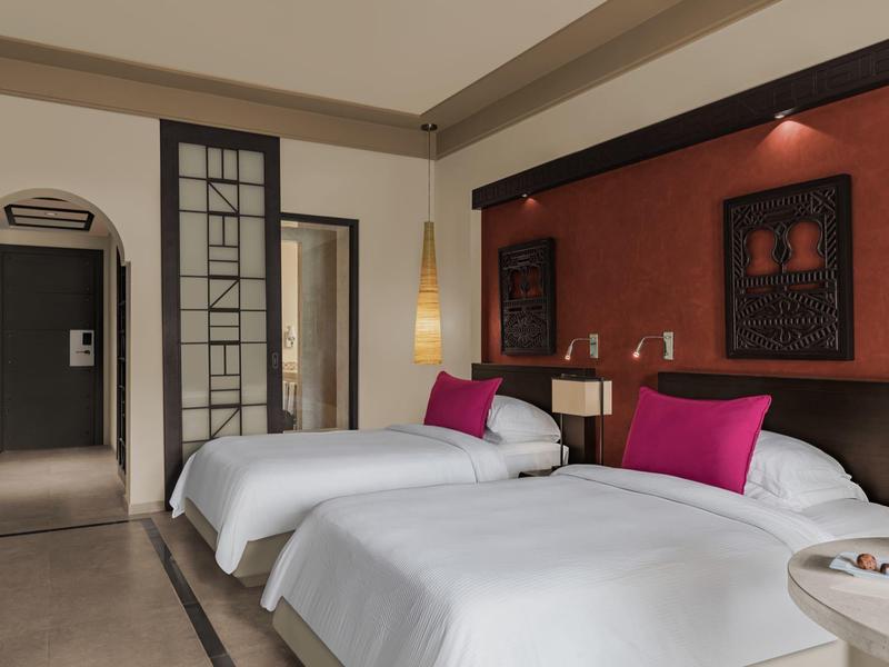 Modernes Schlafzimmer mit zwei Einzelbetten, weißen Bettdecken, pinken Kissen und dekorativer Wandkunst.