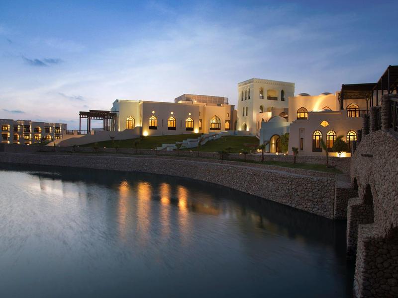 Elegante Gebäude mit warmem Licht am Ufer eines ruhigen Sees bei Abenddämmerung.