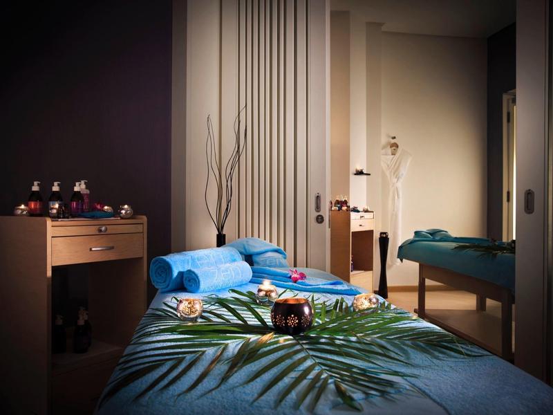 Ein ruhiger, gedämpft beleuchteter Massageraum mit blauem Bett und pflanzlicher Dekoration.