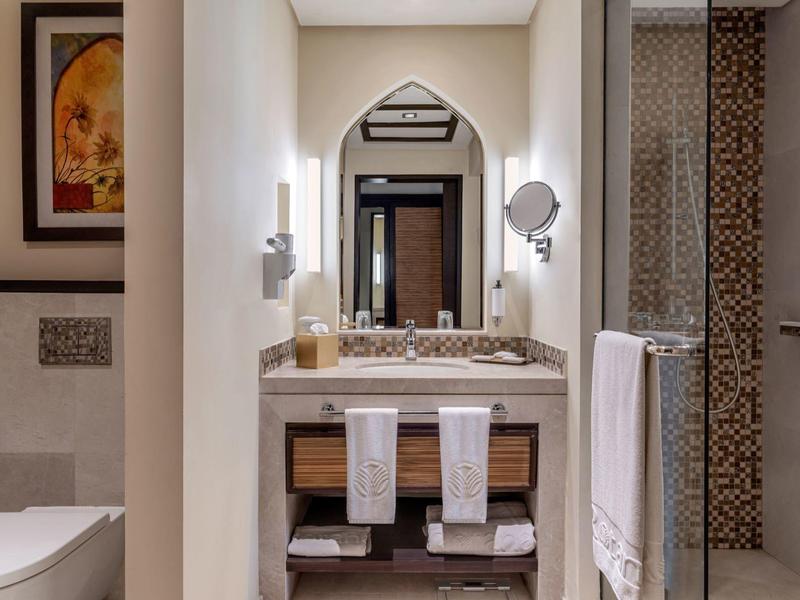 Moderner Badezimmerbereich mit Waschbecken, Spiegel, Handtüchern und Dusche mit braunem Mosaik.