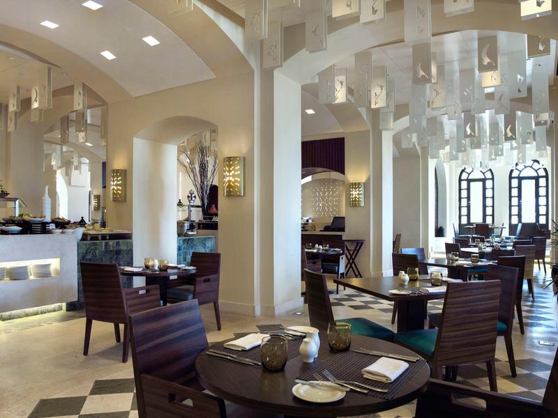 Moderner Speisesaal mit Holztischen, Stühlen, cremefarbenen Wänden und großen Fenstern.