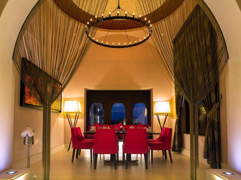 Eleganter Speiseraum mit rotem Stuhlset, hohen Decken, samtigen goldfarbenen Vorhängen und warmem Licht.