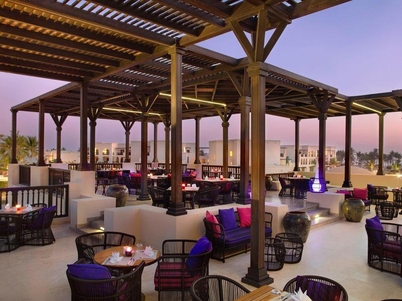 Offener, luxuriöser Außenbereich mit Holzdach, gemütlichen Sitzecken und weichen Sitzkissen bei Sonnenuntergang.