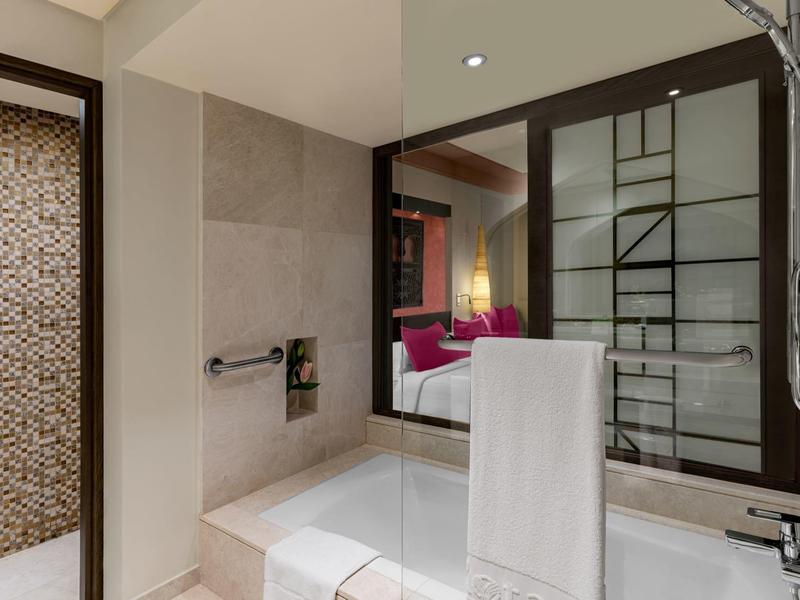 Modernes Badezimmer mit Badewanne, Handtuchhalter, großem Spiegel und Zugang zu einem Schlafzimmer.