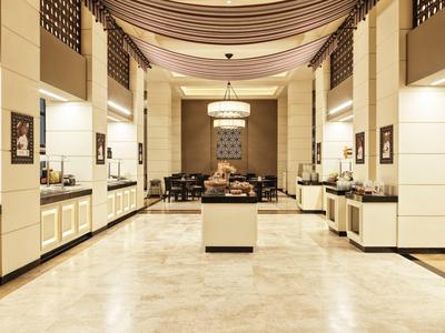 Großer, heller Raum mit poliertem Marmorboden, weiß-beigen Wänden und Buffetstationen an den Seiten.