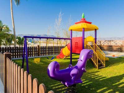 Area giochi colorata con scivolo e altalene in un giardino sotto un cielo sereno.