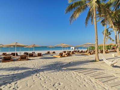 Strand mit Palmen, Sonnenschirmen und Liegestühlen unter blauem Himmel am Meer.