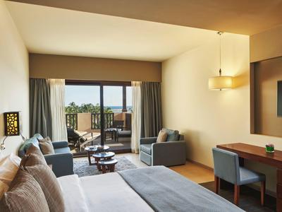 Camera d'hotel moderna con letto, poltrona e balcone con vista su una terrazza.