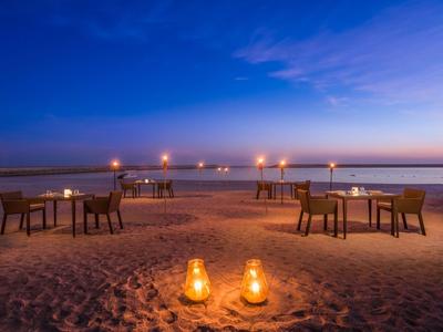 Romantische Strand-Tischdeko bei Sonnenuntergang mit Kerzenlicht und blauem Himmel.