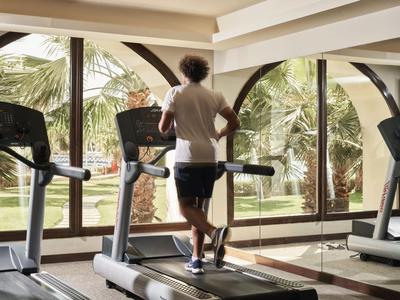 Persona che corre su un tapis roulant in una palestra con grandi finestre che affacciano su palme.