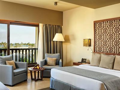 Modernes Schlafzimmer mit großem Bett, zwei Sesseln, Stehlampe und Balkon mit Blick ins Grüne.