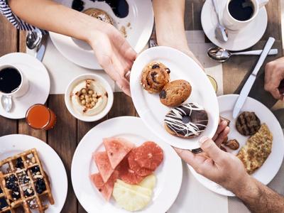 Verschiedene Frühstücksgerichte wie Waffeln, Aufschnitt, Nüsse und Kaffee auf Holztisch.