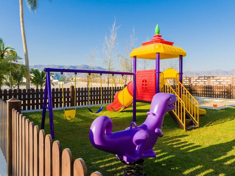 Bunter Kinderspielplatz mit Rutsche, Schaukeln und Klettergerüst auf grünem Rasen im Freien.