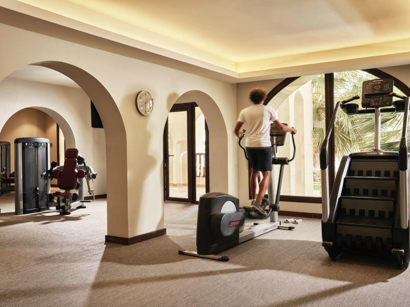 Heller Fitnessraum mit großen Fenstern, Trainingsgeräten und zwei Personen beim Workout.