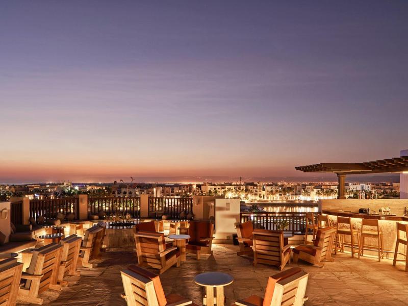 Dachterrasse bei Sonnenuntergang mit Holzstühlen, Tischen und beleuchtetem Barbereich.