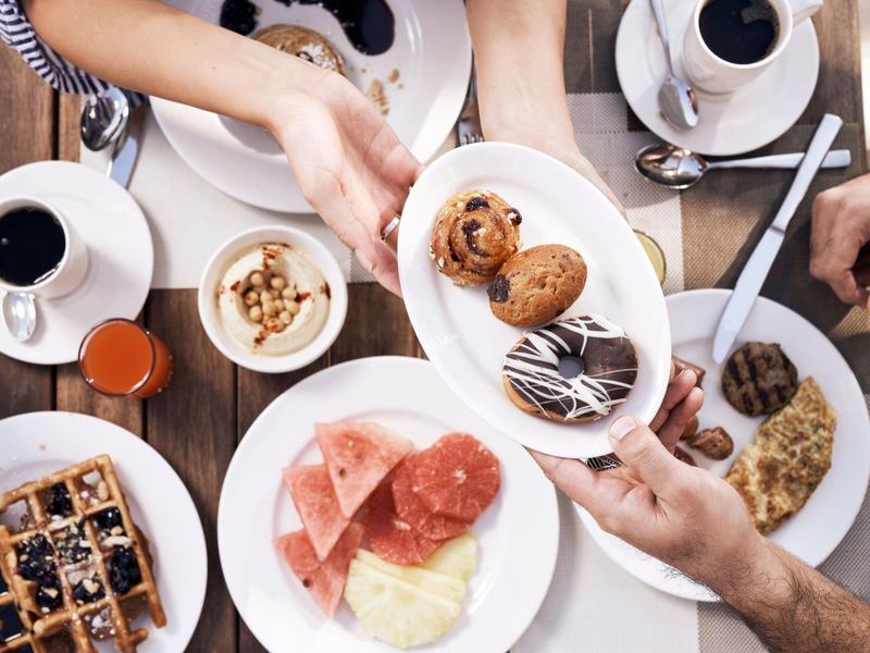 Verschiedene Frühstücksgerichte wie Waffeln, Aufschnitt, Nüsse und Kaffee auf Holztisch.