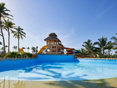 Parco acquatico con scivoli e piscina, circondato da palme sotto un cielo azzurro.