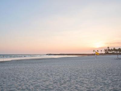 Ampia spiaggia sabbiosa con onde dolci e cielo dai colori pastello al tramonto.