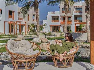 Vrouw ontspant op stoelen in de tuin van een modern hotel met palmbomen en witte gevel.
