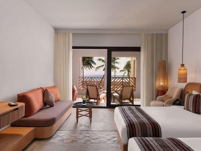 Camera d'hotel moderna con letto matrimoniale, sedie sul balcone e vista sulle palme.