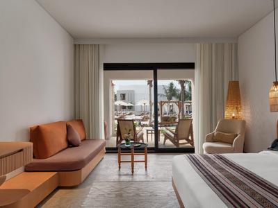 Camera d'hotel moderna con terrazza, divano, sedia e tende chiare.