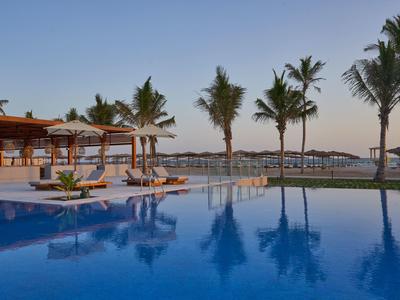Un'area piscina tranquilla con palme e lettini al tramonto.