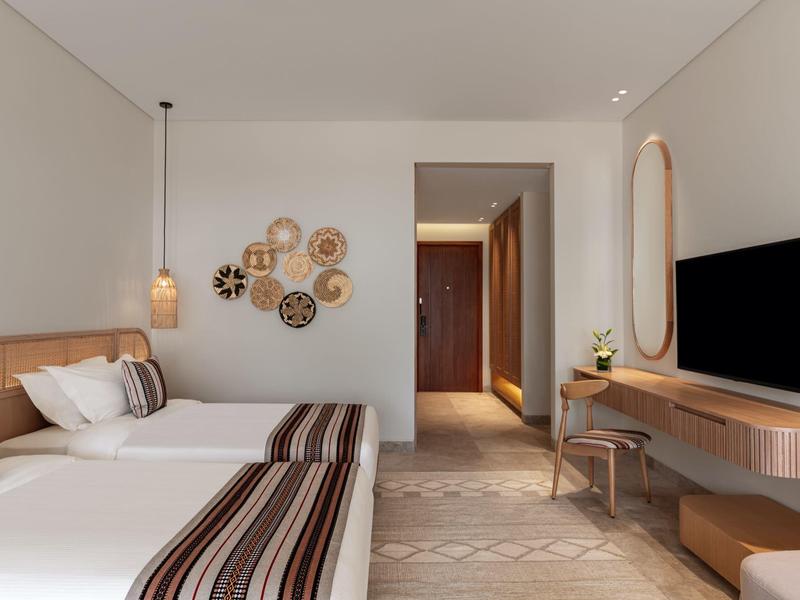 Camera d'hotel moderna con due letti, decorazione murale e TV a parete.