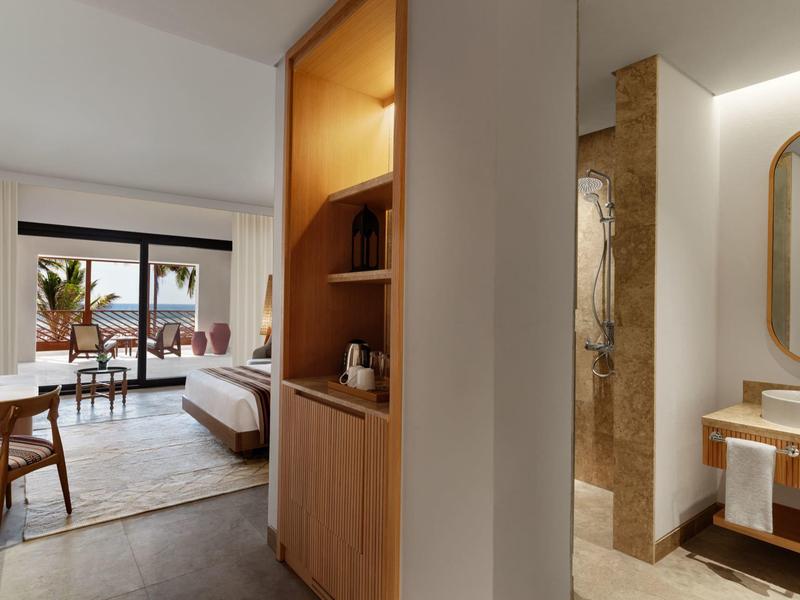 Camera d'hotel moderna con balcone, zona giorno e bagno adiacente con doccia.