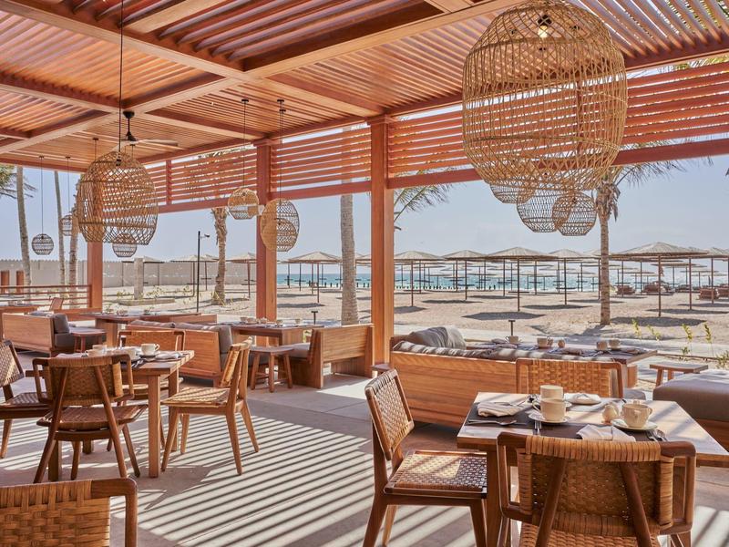 Terrazza in legno aperta con zona pranzo e vista sulla spiaggia e sul mare sullo sfondo.