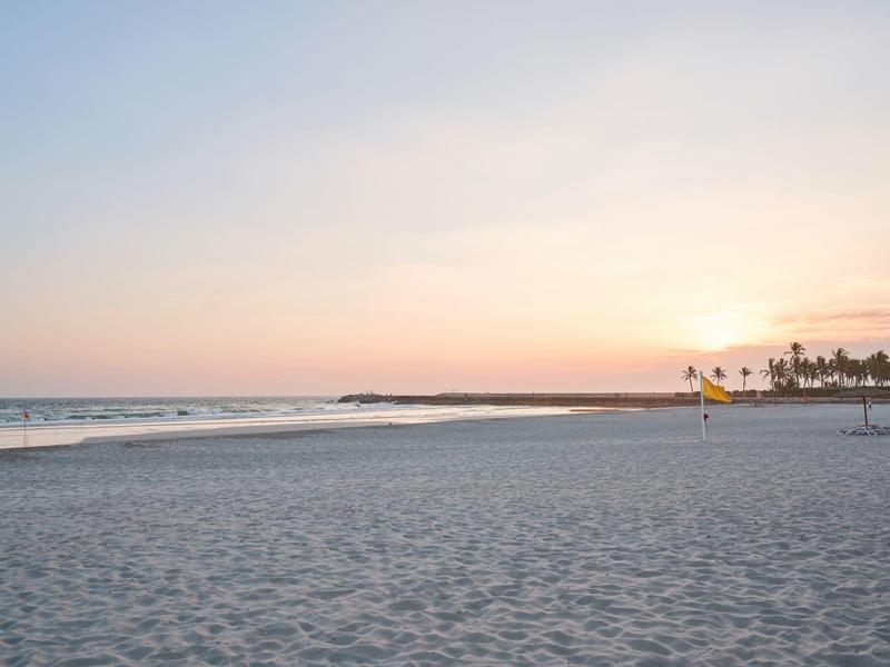 Ampia spiaggia sabbiosa con onde dolci e cielo dai colori pastello al tramonto.