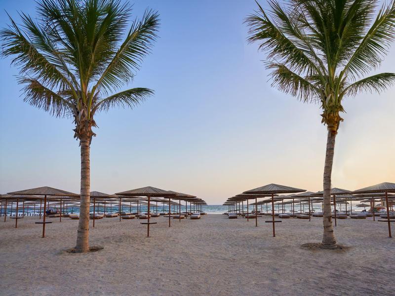 Spiaggia con palme e ombrelloni sotto un cielo limpido.