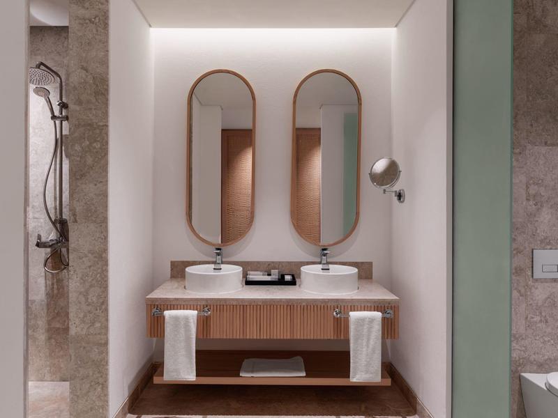 Bagno moderno con due specchi ovali, lavandini e mobili in legno.