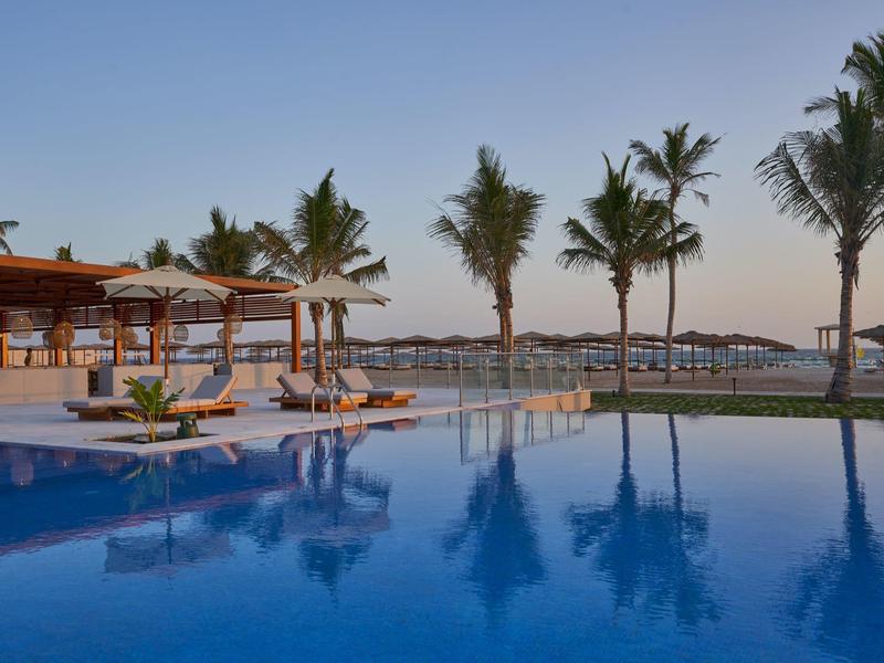 Un'area piscina tranquilla con palme e lettini al tramonto.