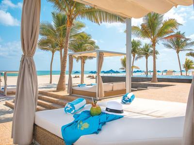 Luxuriöses Strandbett mit Meerblick, umgeben von Palmen und Sonnenschirmen.