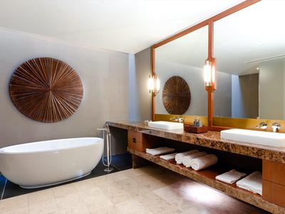 Modern bathroom with free-standing bathtub, large mirror, and wooden shelf with towels.
