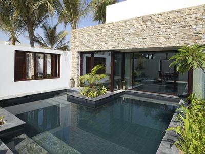 Modern pool area with smooth stone walls and tropical plants at a white house.