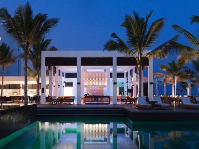 Modernes Hotel bei Nacht mit Pool und Palmen im Vordergrund.