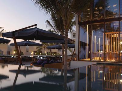 Modern hotel pool area at dusk with palm trees and illuminated glass walls.