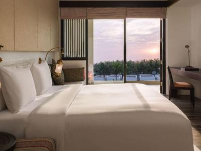 Modern hotel room with large bed, wooden accents, and views of trees at sunset.