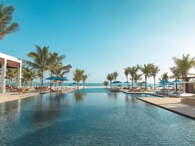 Modern outdoor pool with palm trees and lounge chairs under a clear sky by the sea.