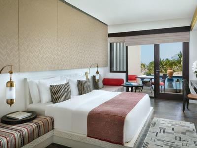Modern hotel room with large bed and balcony overlooking greenery.