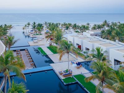 Luxuriöse Hotelanlage mit Pools, Palmen und Blick aufs Meer am Strand.